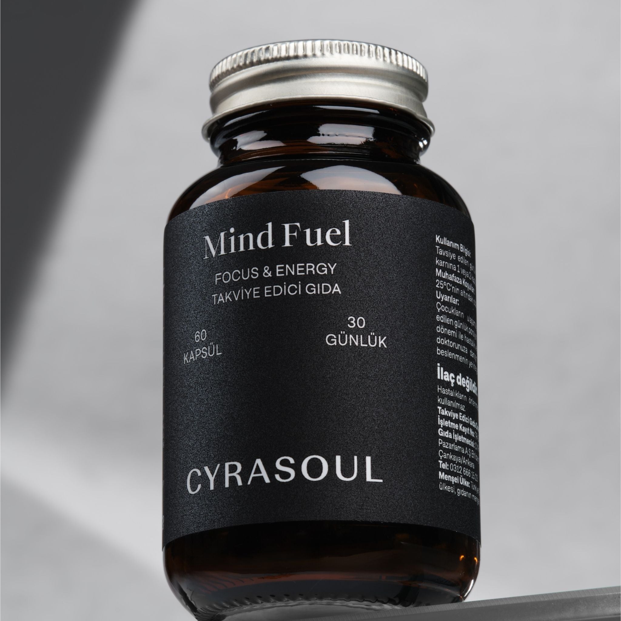 Cyrasoul MindFuel odaklanma ve enerji takviyesinin gümüş kapaklı amber renkli şişesinin profesyonel stüdyo çekimi. Ürünün modern ve şık tasarımı vurgulanıyor.