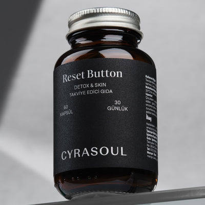 Cyrasoul Reset Button detoks ve cilt takviyesinin gümüş kapaklı amber renkli şişesinin profesyonel stüdyo çekimi. Ürünün premium ve minimalist ambalajı öne çıkıyor.